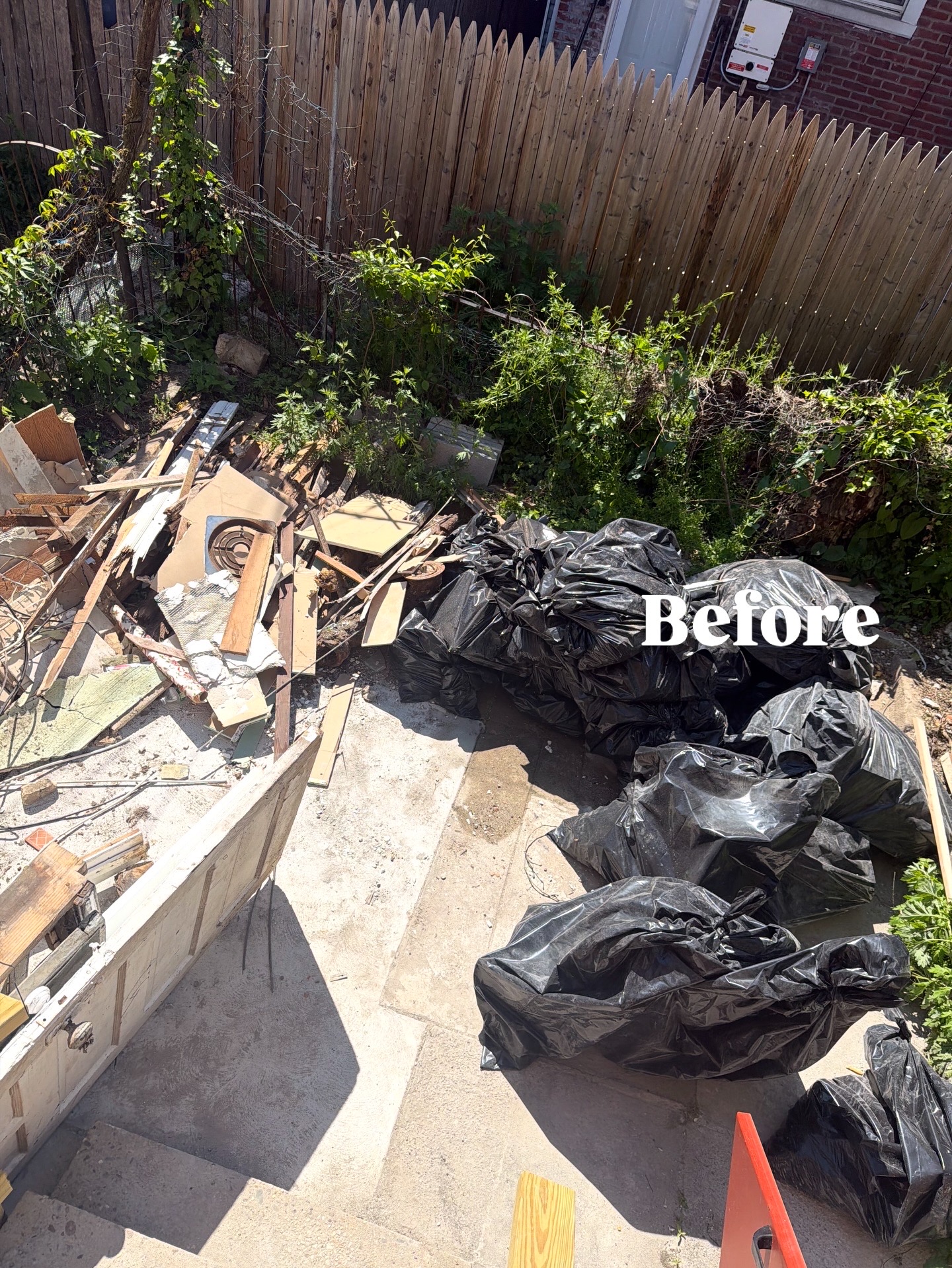 Overgrown Philadelphia backyard filled with construction debris and trash bags before B.L.O.O.M. Entity cleanup
